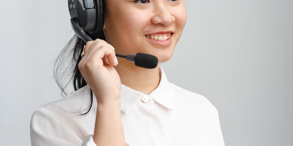 A close-up shot of a customer service representative wearing a headset, smiling while looking at a computer screen displaying a colorful Net Promoter Score dashboard. The background features a vibrant office environment with motivational posters about customer satisfaction.