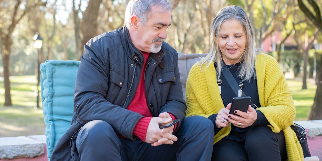 A group of friends gathered in a park, engaging in a lively discussion while holding up their phones, each showing different social media apps. The image captures the essence of real-life connections and the joy of sharing experiences through various platforms, highlighting the alternatives to Facebook.