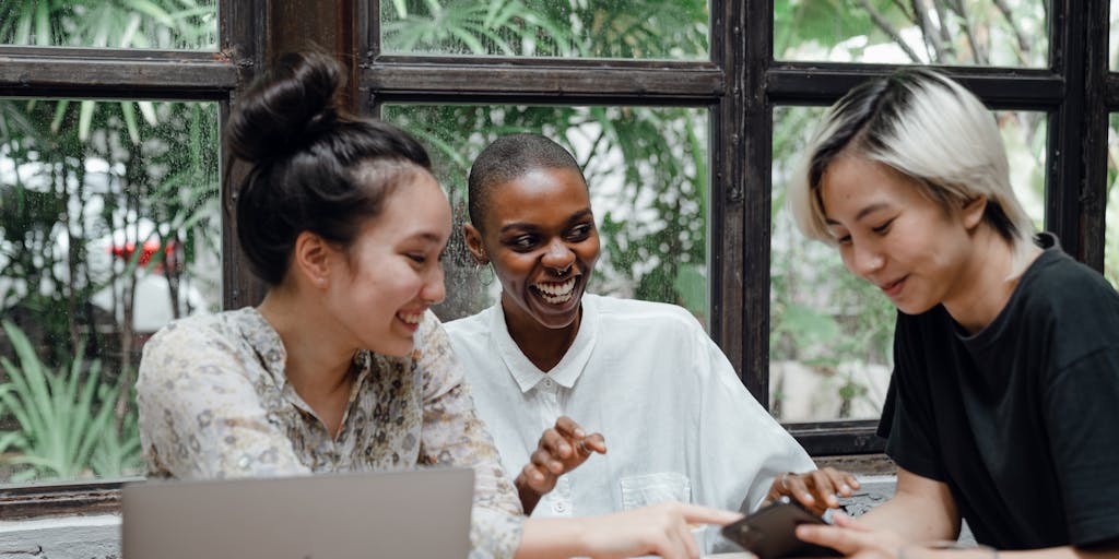 A dynamic photo of a group of diverse young adults engaged in a lively discussion while browsing the Myntra app on their smartphones. The setting is a trendy café with stylish decor, emphasizing the social aspect of shopping. Capture their expressions of excitement and surprise as they discover deals and new arrivals, highlighting Myntra's community-driven marketing approach.