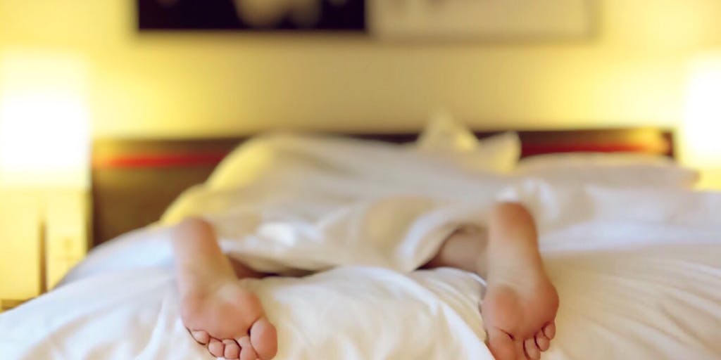 A cozy bedroom scene featuring a Casper mattress with soft, ambient lighting. The bed is adorned with stylish bedding and pillows, and a person is peacefully sleeping, showcasing the comfort and quality of the product. The background includes a nightstand with a book and a cup of herbal tea, emphasizing relaxation and a good night's sleep.