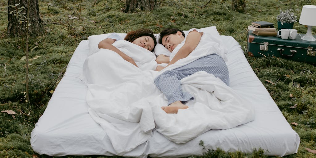 An outdoor picnic setup with a Casper mattress laid out on the grass, surrounded by friends enjoying a sunny day. The scene captures laughter, food, and a sense of community, highlighting the versatility of the mattress for various settings beyond just the bedroom.