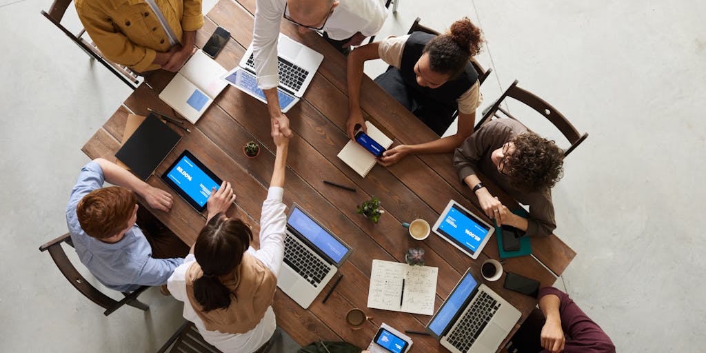 An overhead view of a diverse team gathered around a conference table, with laptops open and DocuSign documents on the screen. The team is engaged in discussion, showcasing collaboration and the efficiency of using DocuSign for business agreements.