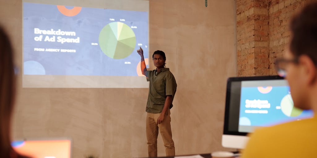 A dynamic image of a marketing professional presenting Okta's marketing strategy to a group of engaged stakeholders. The presenter is using a digital screen to showcase key metrics and strategies, while the audience is actively taking notes and discussing. The setting is a modern conference room with a large window, allowing natural light to illuminate the scene.