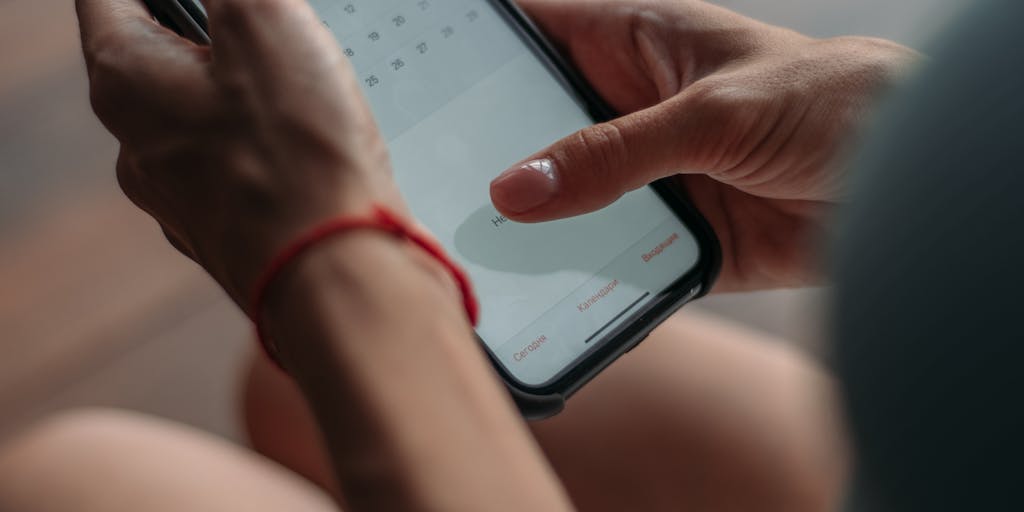 A close-up shot of a smartphone displaying the Calendly app, with a hand tapping on a scheduling link. In the background, a blurred image of a busy office environment conveys the hustle of marketing teams coordinating meetings, highlighting the ease of scheduling through Calendly.