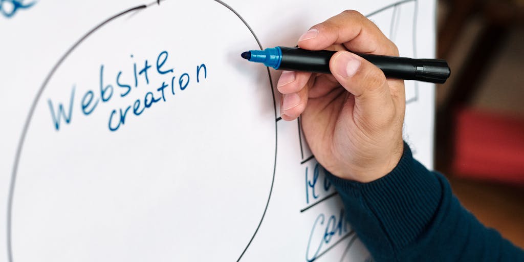 A close-up of a hand writing on a whiteboard filled with marketing strategies and goals, with the Monday.com logo subtly included in the corner. The focus is on the creative process, showcasing the importance of visual planning in marketing.