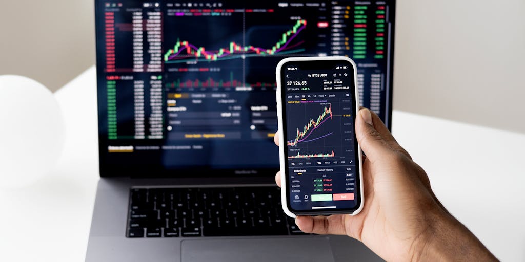 A close-up of a smartphone displaying a QuickBooks Online app notification about a successful marketing campaign. The phone is held in one hand, while the other hand is pointing at a graph on a notepad, symbolizing the connection between digital tools and marketing success.