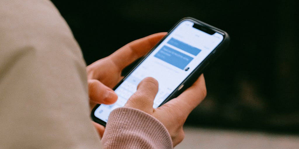 A close-up shot of a smartphone displaying an intercom messaging app interface. The background features a cozy coffee shop setting, with a person casually sipping coffee while interacting with the app. This image captures the essence of mobile marketing and the convenience of intercom communication in everyday life.