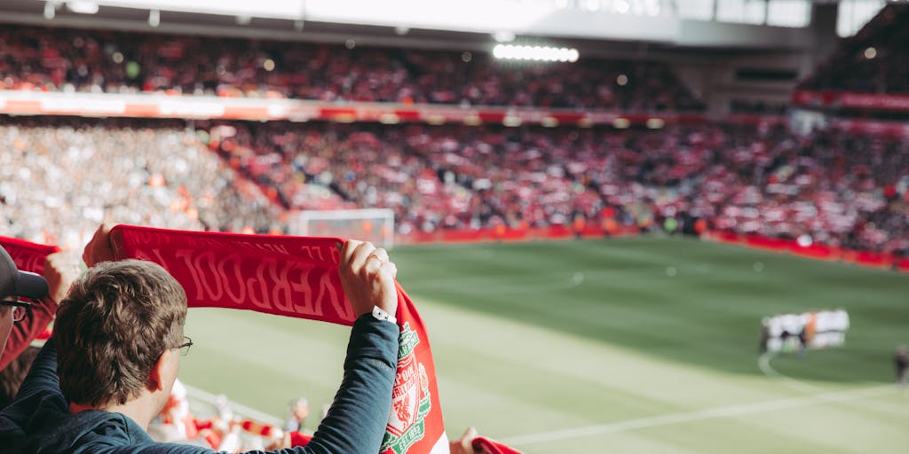 An overhead shot of a packed Anfield stadium during a match, with a sea of red jerseys and flags. The image highlights the electric atmosphere and the emotional connection fans have with the club, showcasing the importance of matchday experiences in Liverpool FC's marketing.