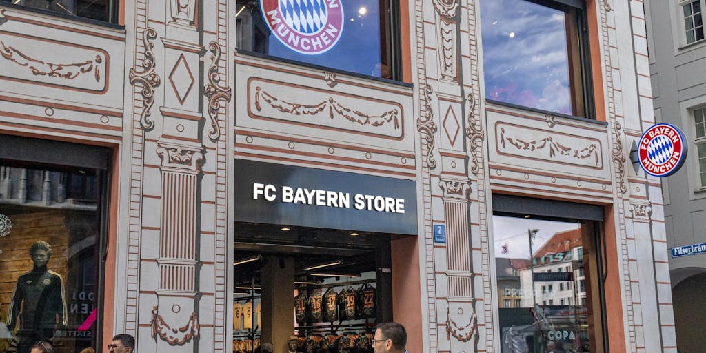 An overhead shot of a bustling Bayern Munich merchandise store filled with fans eagerly shopping for jerseys, scarves, and memorabilia. The photo captures the excitement and energy of fans interacting with the brand, showcasing the club's marketing strategy in retail.