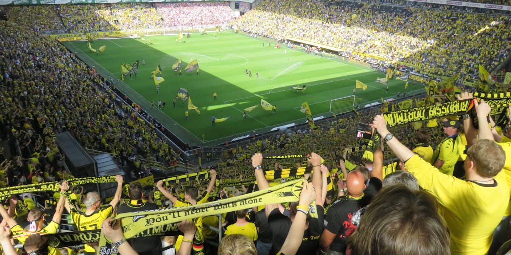 A vibrant photo capturing a group of diverse fans wearing Borussia Dortmund jerseys, holding banners and flags, celebrating in a packed stadium. The energy of the crowd is palpable, showcasing the passionate fan culture that is central to the club's marketing strategy.