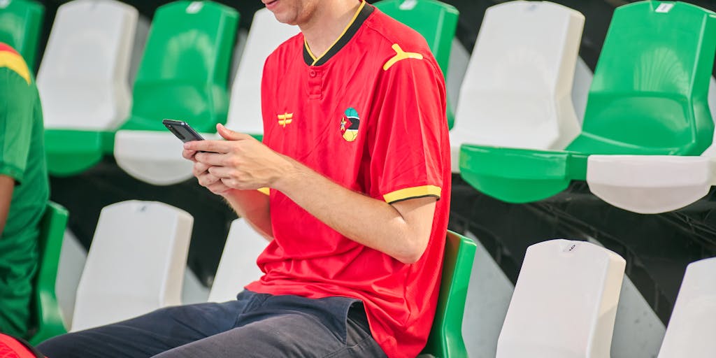 A close-up shot of a smartphone displaying the Zenit Saint Petersburg app, with a fan interacting with it in a stadium seat. The background shows a packed stadium during a match, emphasizing the importance of digital engagement in the team's marketing strategy. The image should capture the excitement of live sports and the role of technology in fan experience.