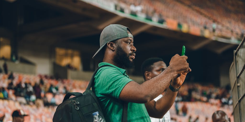 A close-up shot of a young fan holding a smartphone displaying the Corinthians app, with a backdrop of a packed stadium during a match. The photo emphasizes the importance of technology and mobile engagement in the marketing strategy, showcasing how fans can connect with the team through digital platforms.