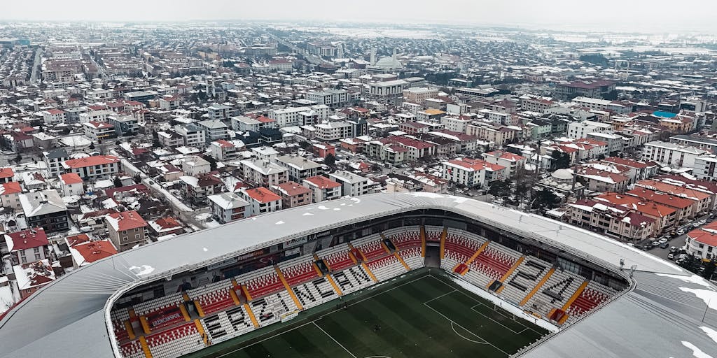 An aerial shot of SoFi Stadium during a game day, with the stadium illuminated and filled with cheering fans. The image captures the excitement and energy of the event, highlighting the Rams' branding throughout the venue, including merchandise stalls and promotional displays.