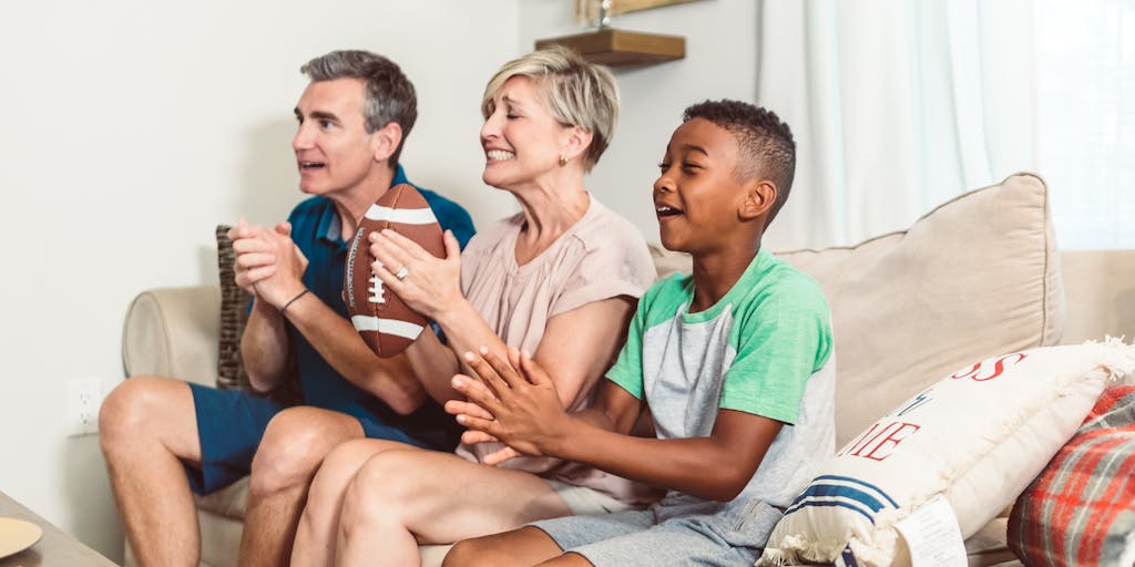 A creative overhead shot of a family watching a New England Patriots game at home, surrounded by themed decorations, snacks, and drinks. The image conveys the idea of family bonding and tradition, aligning with the team's marketing strategy of fostering a sense of belonging and loyalty among fans.