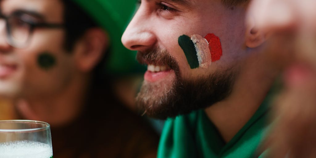 A close-up of a Saints fan painting their face in team colors, surrounded by friends in the background also showing their support. The focus on the fan's expression conveys passion and loyalty, making it a powerful representation of the Saints' marketing strategy to connect emotionally with their audience.