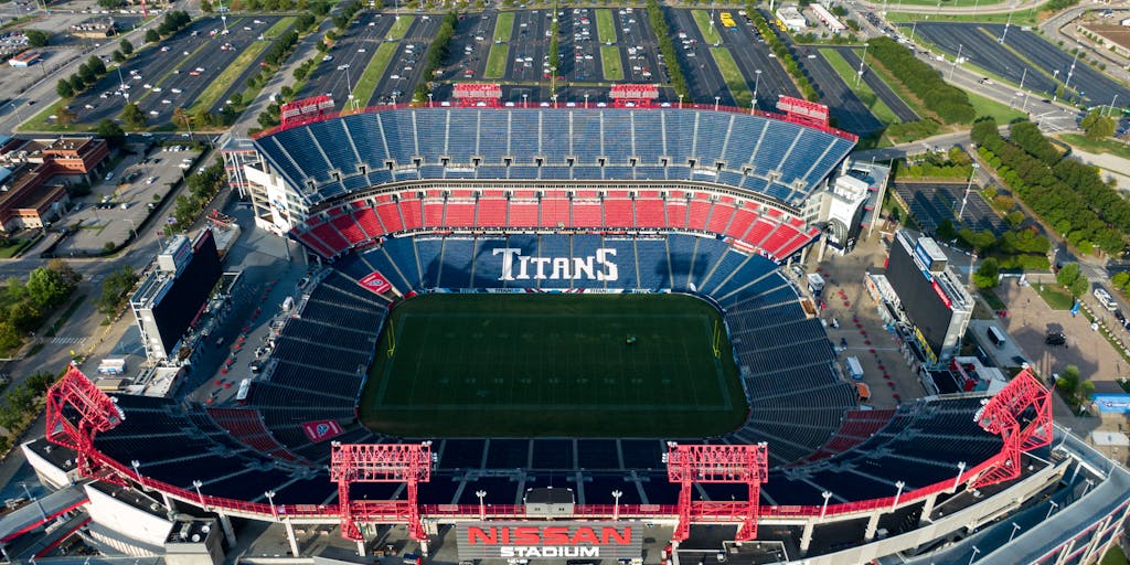 A dynamic shot of a diverse group of fans wearing Tennessee Titans gear, gathered in a vibrant tailgate setting before a game. The background features a large Titans banner and a grill with food, showcasing the community spirit and excitement around the team. This image captures the essence of fan engagement and the social aspect of game day.