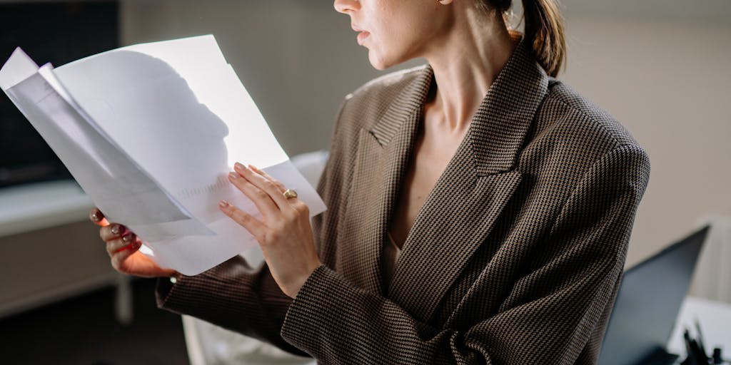 A close-up shot of a person sitting at a desk, intently reviewing emails on a laptop screen. The screen displays the Reachinbox interface, with colorful graphs and statistics visible. The background is softly blurred to emphasize the focus on the screen and the user's expression of concentration.