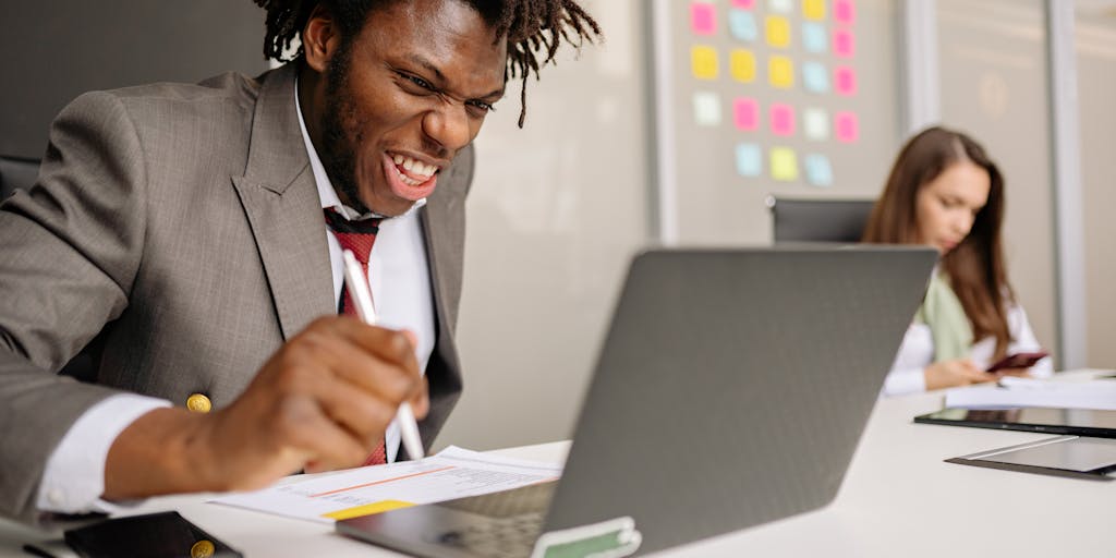 A person sitting at a desk, looking excited while pointing at the screen showing a Lemlist success notification. The background includes motivational posters and a vision board, emphasizing the theme of achieving marketing goals.