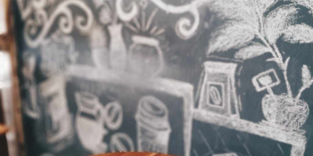 A dynamic image of a barista pouring a perfect latte art with a price list for Dripify services displayed on a chalkboard in the background. The focus is on the latte art, with the chalkboard slightly out of focus to create depth.