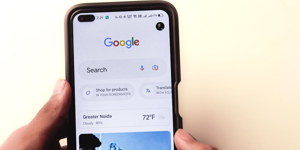 A close-up shot of a hand holding a smartphone displaying the Mailmeteor pricing page, with a blurred background of a cozy home office. The focus is on the screen, highlighting the pricing tiers and features, while the warm lighting creates an inviting atmosphere.