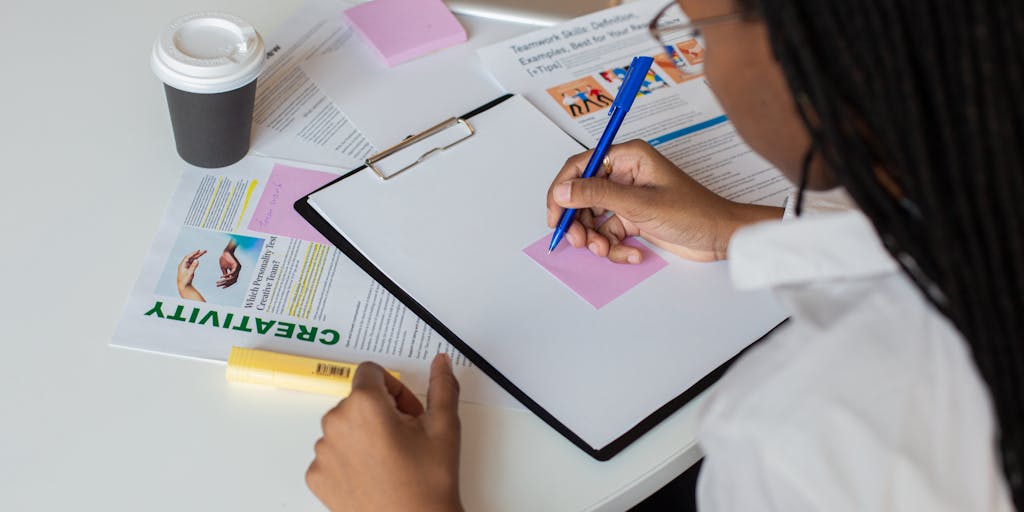 An overhead view of a desk with a laptop open to the Mailmeteor pricing page, surrounded by colorful sticky notes and a cup of coffee. The sticky notes contain handwritten notes about the features and benefits of each pricing tier, adding a personal touch to the workspace.