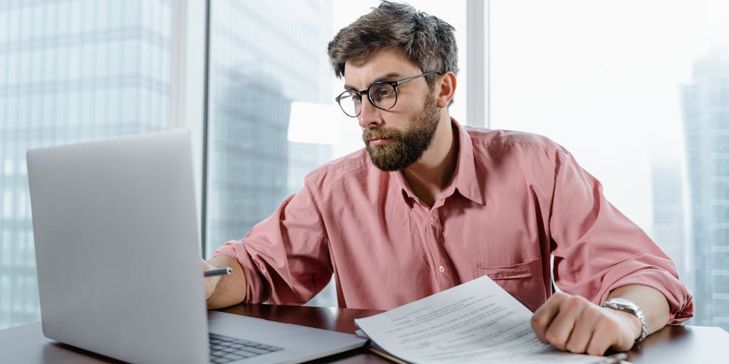 A close-up shot of a laptop screen displaying the Snov.io pricing page, with a person thoughtfully analyzing the options. The setting should be a modern workspace with plants and a coffee cup to create a productive vibe.