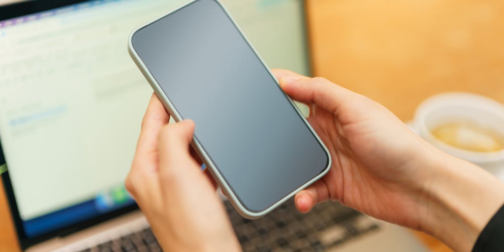 A close-up shot of a smartphone displaying an email app with a pricing table open on the screen. The background features a cozy coffee shop setting, with a steaming cup of coffee and a notepad, suggesting a casual yet professional atmosphere for discussing pricing.