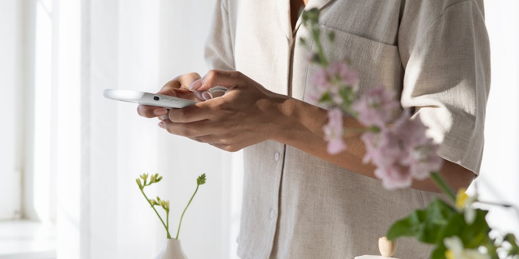 A close-up shot of a hand holding a smartphone displaying the Findymail pricing page, with a blurred background of a coffee shop setting. The focus on the phone emphasizes the ease of accessing pricing information on-the-go.