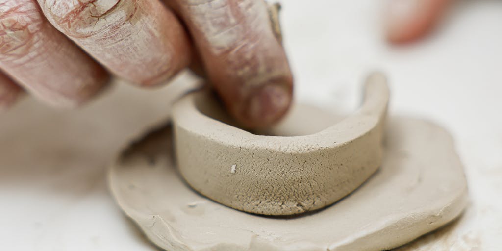 A close-up shot of a hand sculpting a piece of clay, with a price tag hanging from the clay block. The background is softly blurred to emphasize the craftsmanship and the price tag, symbolizing the value of handmade art.