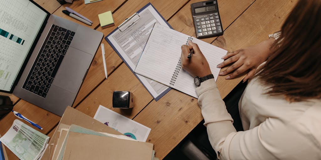 An overhead view of a workspace with a laptop open to the Yet Another Mail Merge pricing page. Surrounding the laptop are various envelopes, stamps, and a calculator, symbolizing the merging of digital and traditional mailing methods.