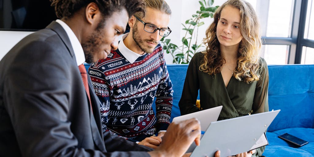 An overhead view of a diverse group of people sitting around a table, engaged in a brainstorming session about customer pricing strategies. Various documents, laptops, and coffee cups are scattered across the table, creating a dynamic and collaborative atmosphere.