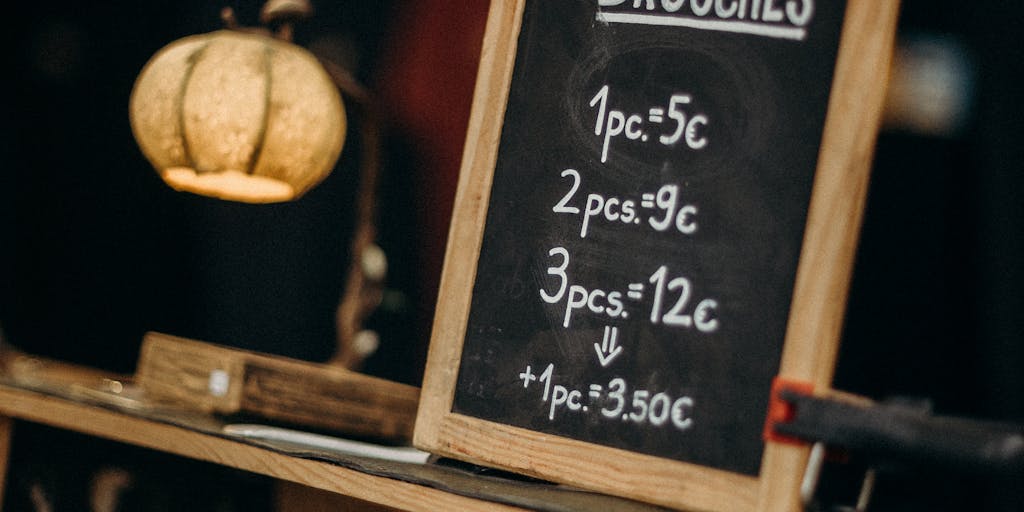 A creative flat lay of a chalkboard with hand-drawn illustrations of canaries and pricing tiers. Next to the chalkboard, there are colorful feathers and small envelopes, giving a playful and artistic vibe to the concept of pricing.