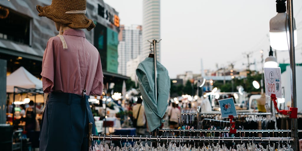 An overhead shot of a busy marketplace where vendors are displaying their products with various price tags. In the center, a large sign reads 'Merge Pricing' with arrows pointing to different products, illustrating the idea of combining prices for better deals.