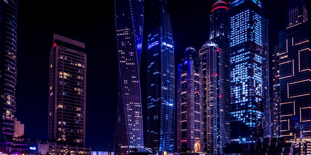 A futuristic city skyline at dusk, with vibrant neon lights illuminating the buildings. In the foreground, a diverse group of people are gathered around a digital display showcasing the 'Apollo Pricing Unlimited' logo, symbolizing innovation and community engagement in technology.