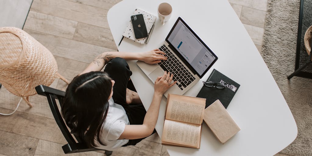 An overhead shot of a desk cluttered with SEO tools, notebooks, and a cup of coffee, with a laptop screen displaying the Outrank.so dashboard. This conveys a sense of productivity and the tools needed for effective SEO management.