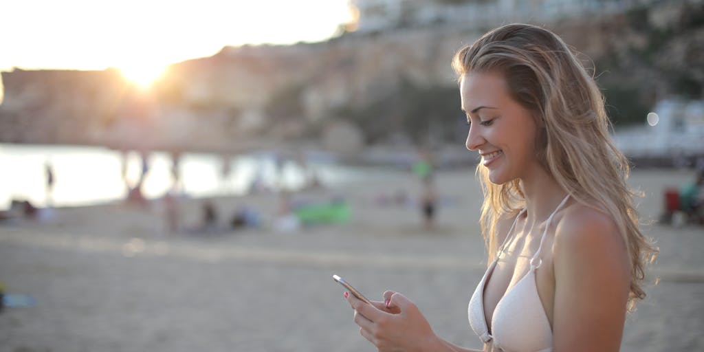 A vibrant beach scene at sunrise, featuring a surfer checking their smartphone on the sand while their surfboard stands upright beside them. The ocean waves crash in the background, and the warm colors of the sunrise reflect on the water, symbolizing the blend of surfing and digital marketing.