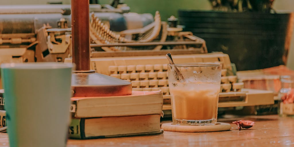 A cozy writing nook featuring a vintage typewriter surrounded by stacks of books, a steaming cup of coffee, and a window with soft natural light streaming in. The scene captures the essence of a writer's retreat, emphasizing creativity and inspiration.