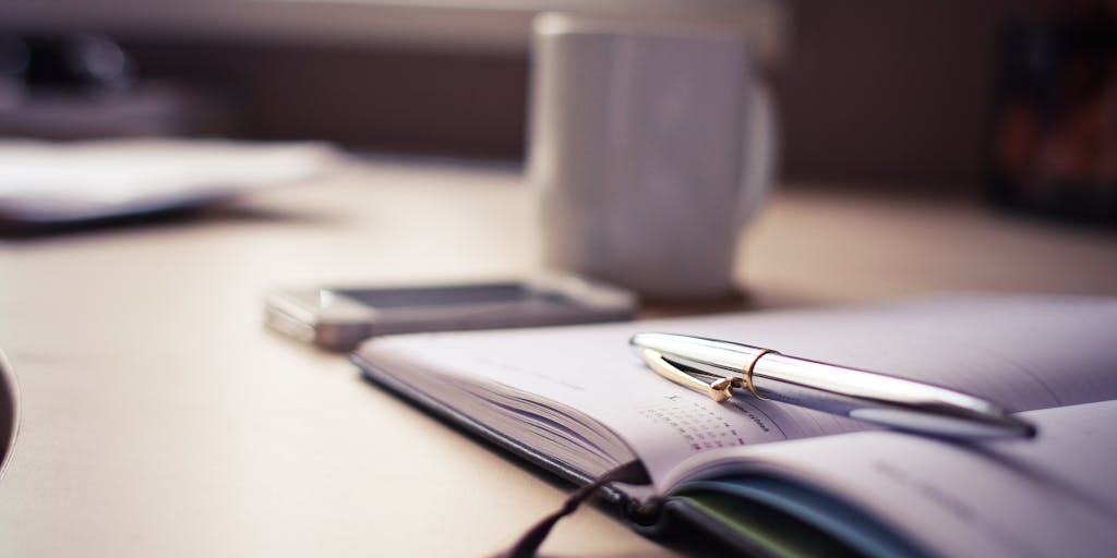 An overhead shot of a workspace filled with various writing tools, including notebooks, pens, and a laptop displaying a vibrant interface of a CopyAI alternative. The scene is well-lit, with a coffee cup and a plant to add a cozy touch.