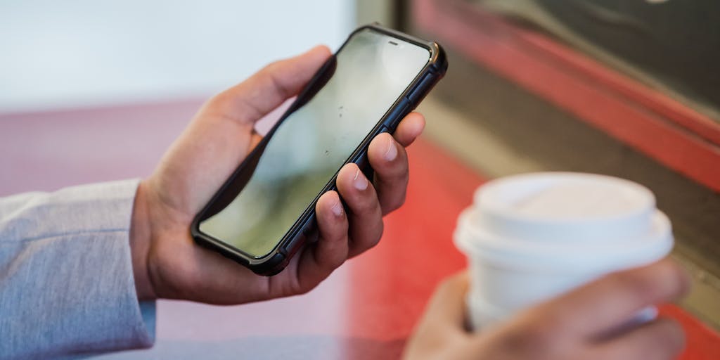 A close-up shot of a hand holding a smartphone displaying a writing app alternative to Anyword, with a blurred background of a bustling café. The focus should be on the screen, showcasing the app's features, while the café ambiance adds a lively touch.