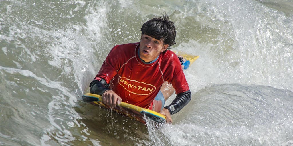 A dynamic action shot of two surfers competing in a friendly race on a beach, with one surfer wearing a jersey with the Surfer SEO logo and the other with the Clearscope logo. The background features a cheering crowd of digital marketers holding signs with SEO tips, creating an engaging atmosphere of competition and collaboration.
