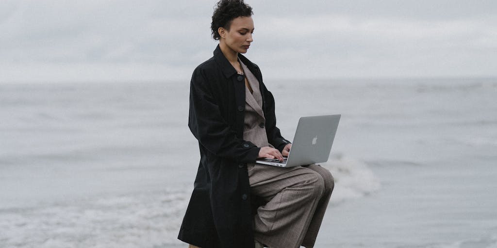 A conceptual photo of a surfer and a business professional standing back-to-back on a beach, each holding tools of their trade: the surfer with a surfboard and the professional with a laptop. The ocean waves behind them are filled with SEO-related icons, while the sky above transitions from a sunny day to a digital cloud, symbolizing the blend of creativity and technology.