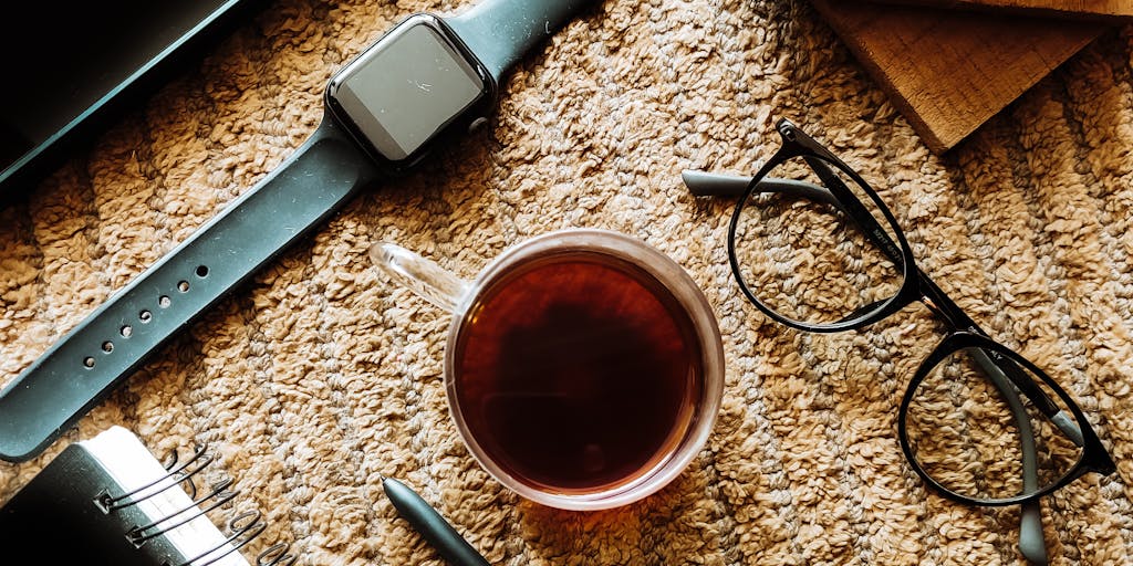 An overhead shot of a person using a tablet to analyze social media metrics on Zoho Social, with a notepad and pen beside them. The background includes a plant and a cozy blanket, creating a warm and inviting atmosphere for digital marketing.