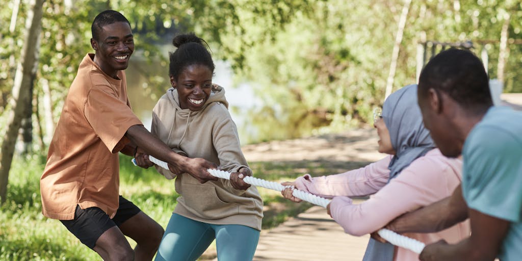An artistic representation of a tug-of-war between two teams, one wearing Agorapulse branded shirts and the other in Publer gear. The rope symbolizes social media engagement, with various social media icons floating around them. This dynamic image captures the competitive spirit between the two platforms.