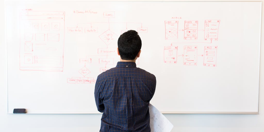 A dynamic action shot of a person standing in front of a large whiteboard, drawing a flowchart that compares the features of SocialBee and FeedHive. The person is animatedly explaining the differences, with sticky notes and colorful markers scattered around, creating an engaging visual representation of the competition between the two services.