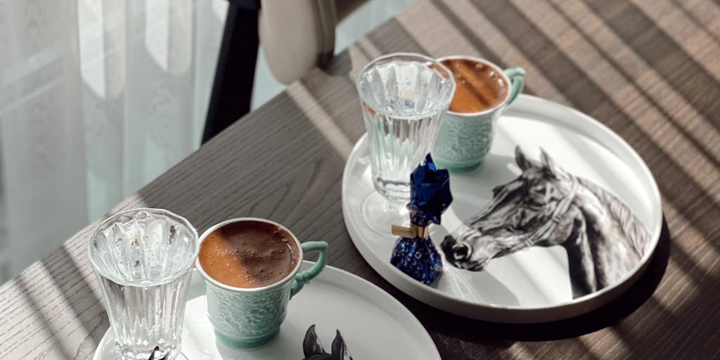 An overhead shot of two coffee cups on a table, one labeled 'Agorapulse' and the other 'Buffer'. Between them, a notepad with pros and cons written down for each platform. The scene is cozy and inviting, suggesting a casual discussion about the two social media management tools over coffee.
