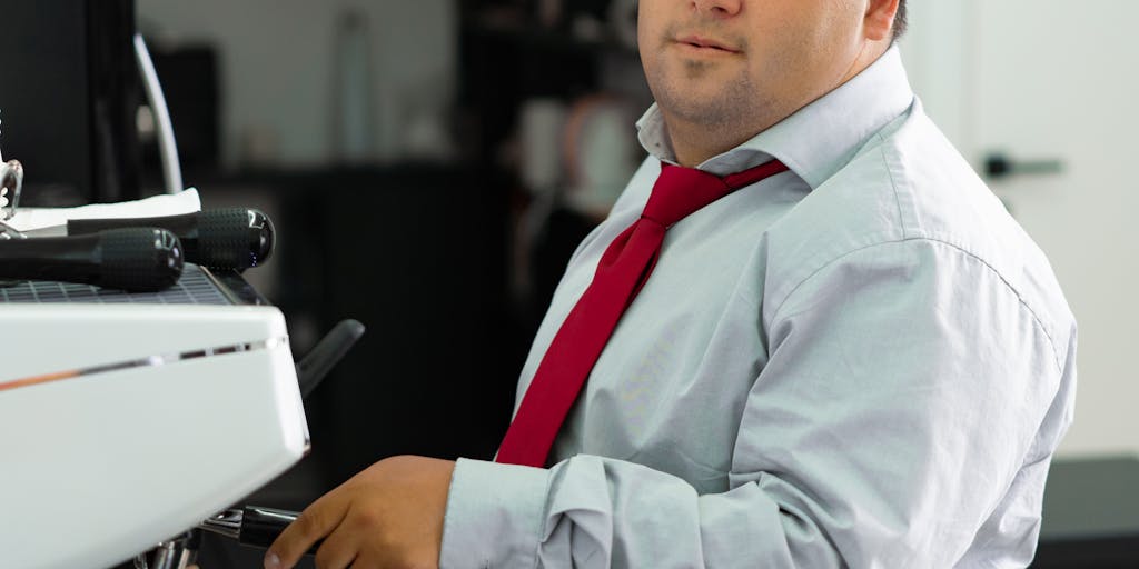 A split-screen image showing two desks side by side. On one side, a person is using Zoho Social with a laptop displaying its dashboard, surrounded by Zoho branding elements like colors and logos. On the other side, another person is using SocialPilot with a similar setup, showcasing its interface and branding. The background should be a vibrant office space to convey a modern work environment.