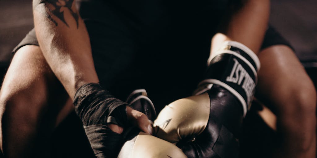 An artistic representation of a boxing ring where Metricool and Agorapulse are personified as cartoon characters, each wearing boxing gloves and standing in their respective corners. The background features a cheering crowd of social media icons, symbolizing the competition between the two platforms.