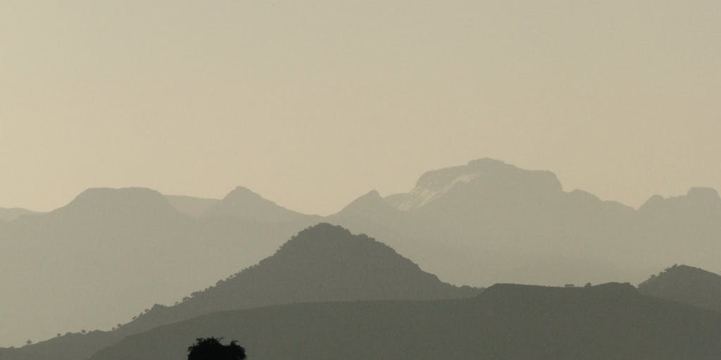 An artistic representation of a digital landscape where the logos of Vista Social and Metricool are depicted as two distinct mountains. A group of diverse professionals is seen hiking towards each mountain, symbolizing the journey of choosing the right social media tool for their needs.