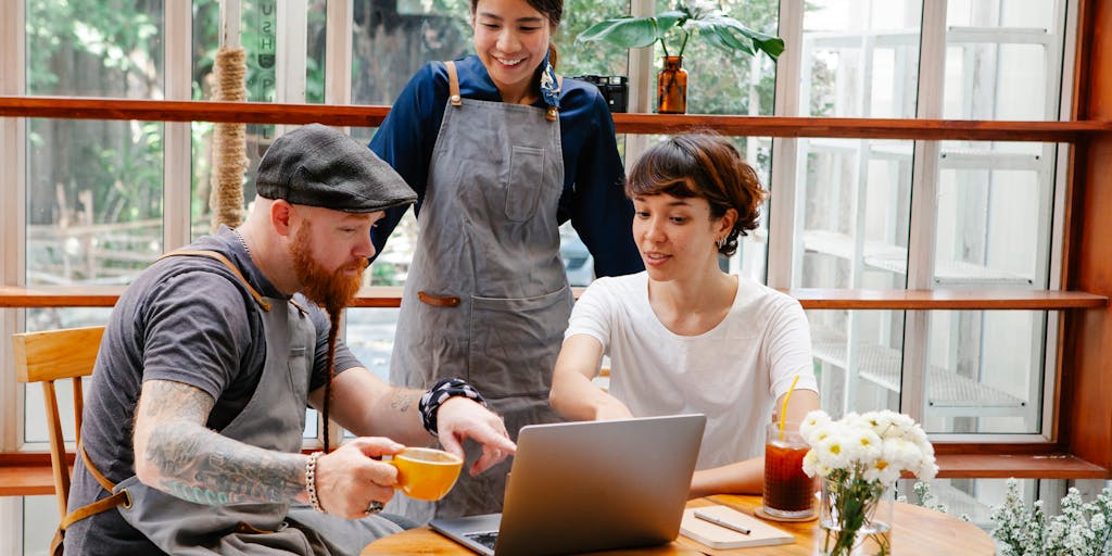 A dynamic action shot of a person using both ContentStudio and Zoho Social on two different devices (tablet and laptop) in a vibrant coffee shop setting. Capture the person engaged in content creation, with a focus on their expressions and the devices, highlighting the multitasking aspect of social media management.