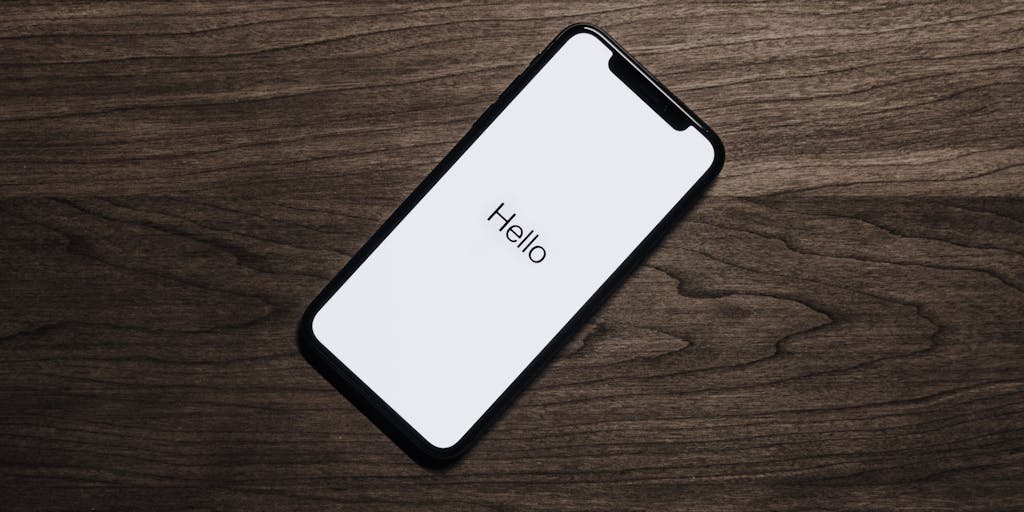 A close-up shot of two smartphones side by side, each displaying the user interface of Vista Social and Zoho Social. The phones are placed on a wooden table with coffee cups and notebooks around them, suggesting a brainstorming session. The focus is on the screens, highlighting the differences in design and functionality.